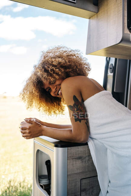 Relaxed African American female with mug of hot drink and chilling inside modern RV in summer morning — Stock Photo