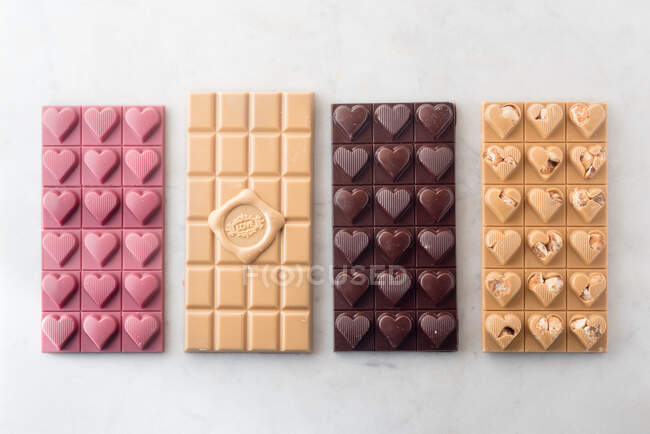 Desde arriba de deliciosas barras de chocolate coloridas colocadas en fila sobre fondo blanco - foto de stock