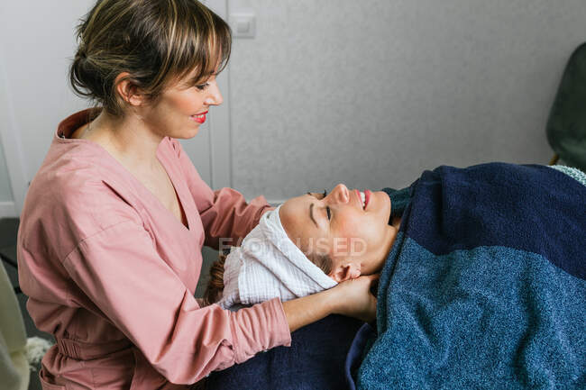 Vista lateral do conteúdo massagista massageando ombros de cliente feminino deitado na mesa no salão de beleza — Fotografia de Stock