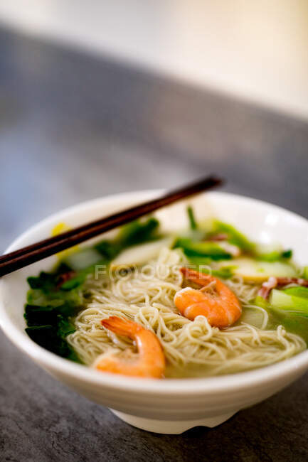 From above hand eating bowl of tasty seafood noodles with chopsticks on black wooden table in Asian cafe — Stock Photo