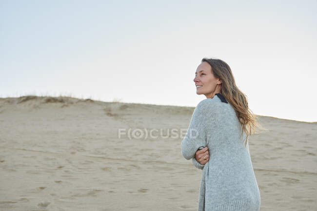 Zufriedene Weibchen in warmer Kleidung stehen am Strand am Meer und genießen den Sommerabend, während sie wegschauen — Stockfoto