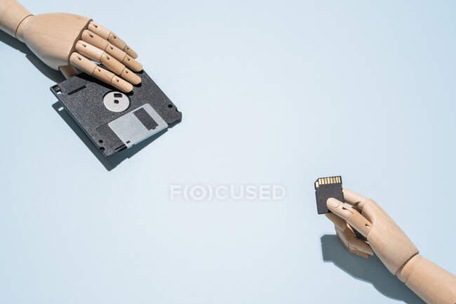 De arriba del disquete grande pasado de moda y la tarjeta de memoria pequeña contemporánea en las manos de madera colocadas sobre el fondo azul claro - foto de stock