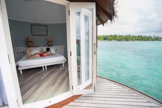 Seitenansicht einer Frau im Badeanzug, die sich auf dem Bett im Hotel der Malediven lehnt — Stockfoto