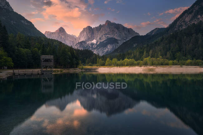 Magnífico paisaje de estanque tranquilo rodeado de montañas bajo el cielo del atardecer en Eslovenia - foto de stock