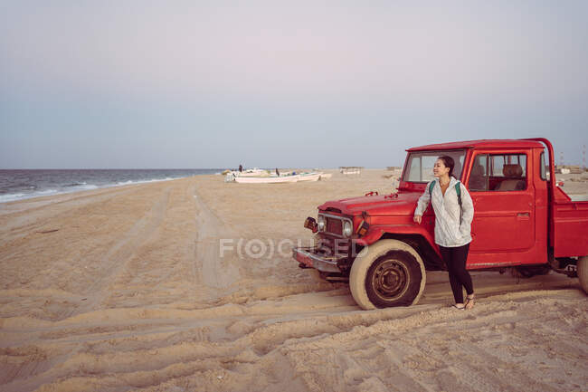 Donna asiatica appoggiata ad una macchina rossa sulla spiaggia di Turtle Beach, Sud, Oman — Foto stock