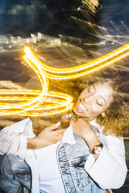 Joyeux jeune homme afro-américain donnant tour de dos à une petite amie heureuse avec les cheveux bouclés dans une tenue à la mode près des lumières de gel — Photo de stock