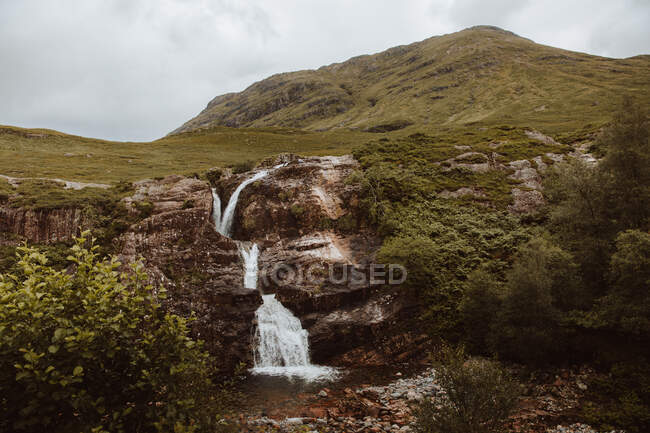 Picturesque view of small waterfall in rocks and ferns in mountain valley of Glencoe in United kingdom on summertime — Stock Photo