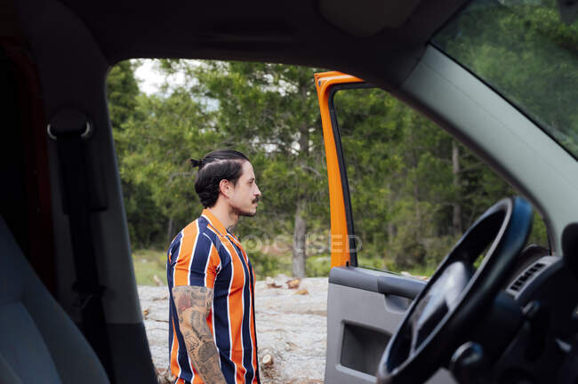 Side view of male traveler standing near opened door of van parked in woods in summer — Stock Photo