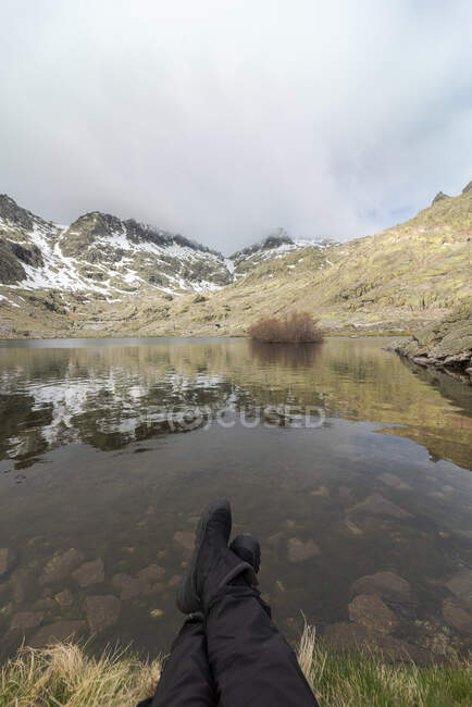 POV de turista anônimo descansando na costa da pacífica Laguna Grande lago no Circo de Gredos circo cercado com montanhas nevadas em Ávila, Espanha — Fotografia de Stock