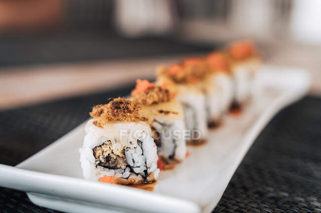 Ряд вкусных суши-роллов с вареным рисом и ломтиками морепродуктов на керамической тарелке на столе — стоковое фото