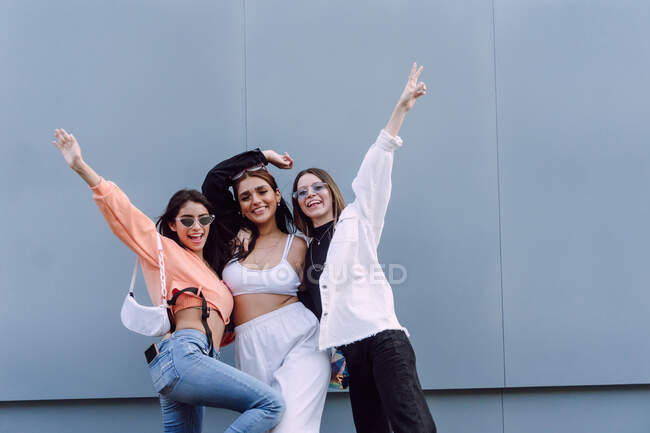 Amigos femininos positivos em óculos de sol da moda e roupas casuais rindo alegremente enquanto passam um tempo agradável juntos — Fotografia de Stock
