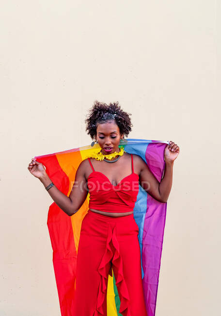 Stylish African American female in trendy clothes with colorful flag looking down during celebration — Stock Photo