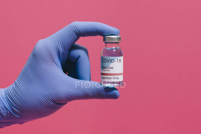 Cropped unrecognizable doctor's hand holding showing coronavirus vaccine flask on pink background — Stock Photo