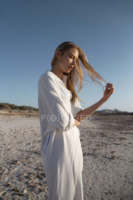 Mujer rubia con el pelo largo de pie en la playa mirando hacia otro lado - foto de stock