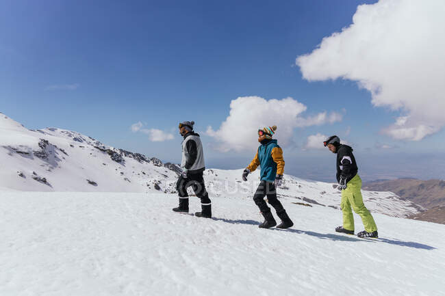 Бічний вид спортсменів у окулярах, що сходять у снігову гору під хмарним блакитним небом у провінції Гранада (Іспанія). — стокове фото