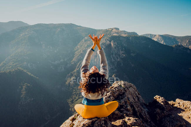 Vista posterior de una viajera anónima sentada en roca en las tierras altas y haciendo yoga en Padmasana - foto de stock