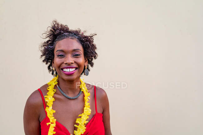 Счастливая афроамериканка, стоящая у белой стены и смотрящая в камеру — стоковое фото