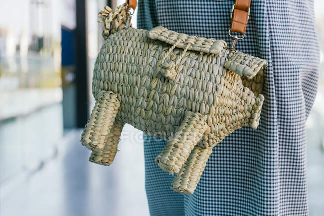Unrecognizable crop fashionable person with wicker handbag in shape of pig standing in city street — Stock Photo