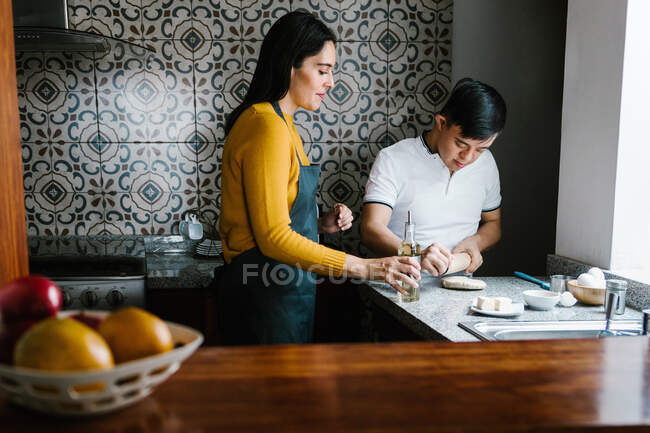 Любить этнических матерей и подростков с синдромом Дауна, готовящих тесто вместе на кухне дома — стоковое фото