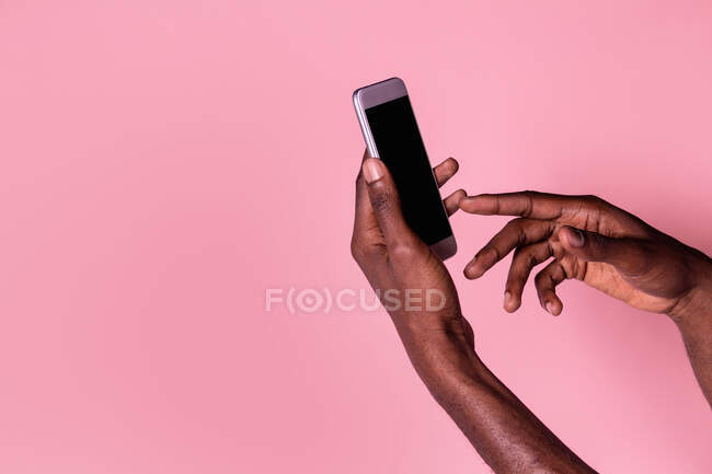 Crop hands of african american man holding phone with blank screen and doing gesture isolated on pink background — Stock Photo