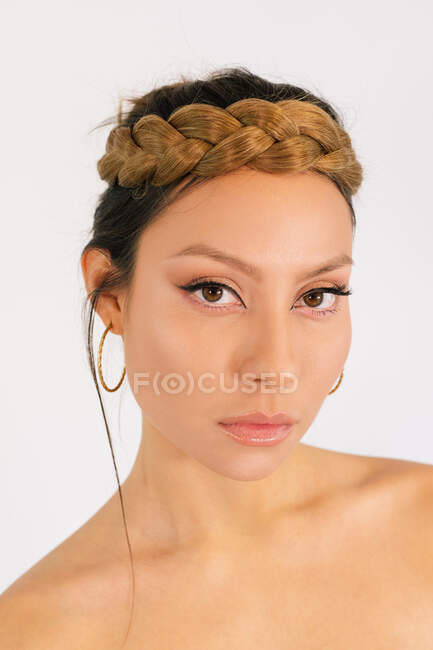 Hermoso modelo femenino joven con elegante peinado trenzado y maquillaje y  con pendientes de aro de oro sobre fondo blanco mirando a la cámara —  ocasión, Bohemio - Stock Photo | #517117100