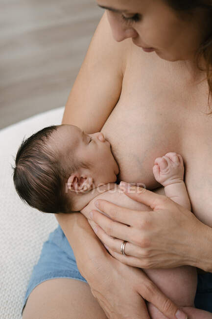 Cropped unrecognizable loving mother breastfeeding newborn while sitting in room at home — Stock Photo