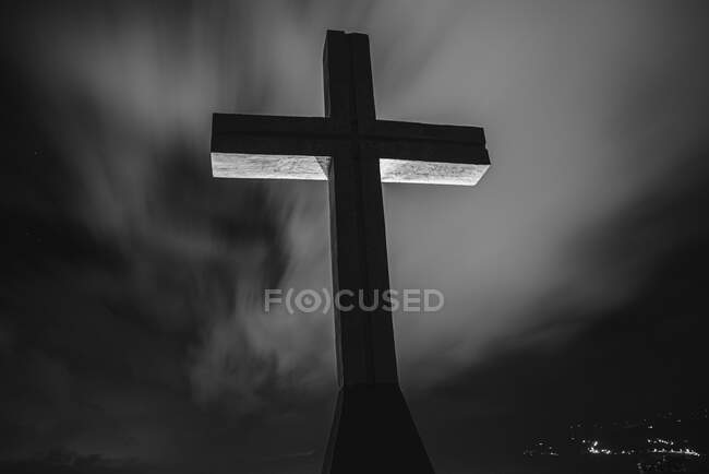 Da sotto monumento di una croce con sfondo di nuvole nel buio — Foto stock