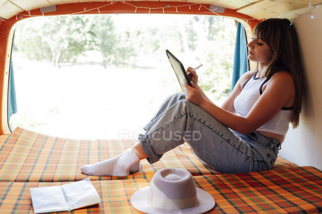 Exploratrice calme assise sur le lit en van et surfant sur Internet sur tablette pendant le voyage d'été — Photo de stock