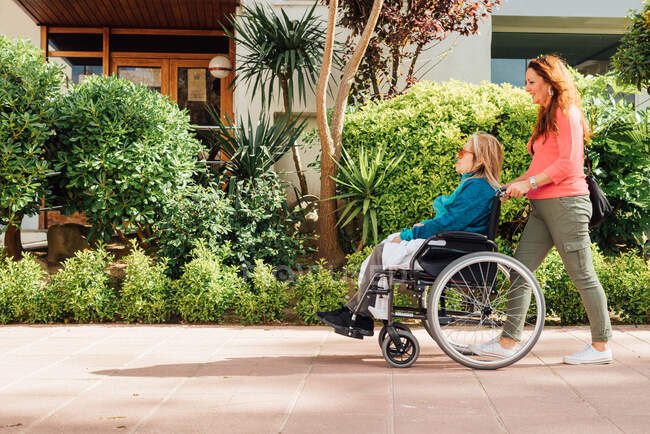 Vista lateral da mãe idosa em cadeira de rodas e filha adulta andando juntas na rua — Fotografia de Stock