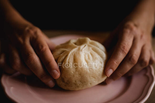 Руки женщины средних лет, кладущей на керамическую тарелку булочку с баози на пару — стоковое фото
