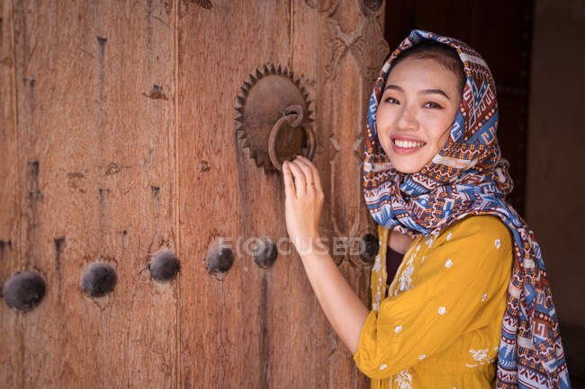 Mulher asiática com lenço de cabeça ao lado de uma velha porta de madeira — Fotografia de Stock