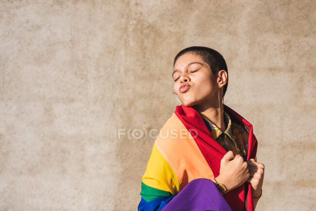 Contenido joven bisexual étnica femenina con los ojos cerrados y bandera multicolor que representa símbolos LGBTQ en el día soleado - foto de stock