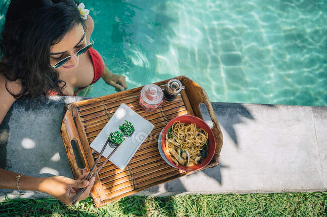 De cima de cultura turista feminina na piscina com saborosos rolos de sushi gunkan com chuka entre pauzinhos durante a viagem de verão — Fotografia de Stock