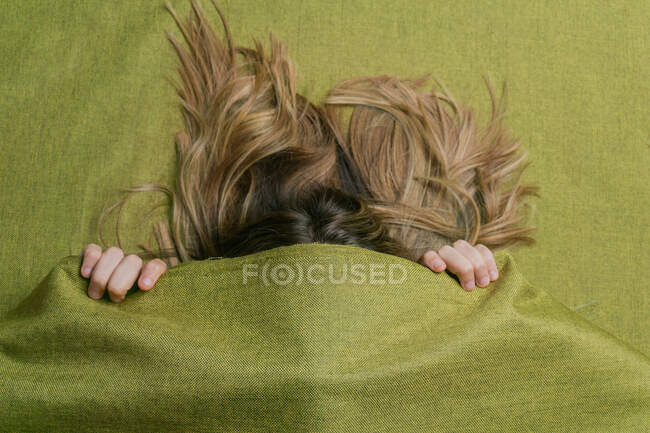 Сверху анонимная женщина с длинными светлыми волосами, покрывающими лицо зеленой тканью — стоковое фото