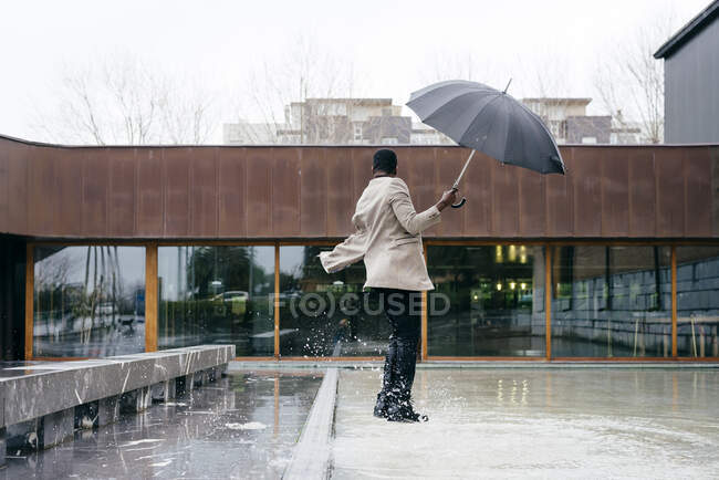 Портрет элегантного черного мужчины в сером пальто и зонтике на улице — стоковое фото
