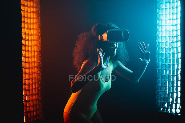 Anonimo stupito femmina etnica con la bocca aperta esplorare realtà virtuale in cuffia su sfondo nero — Foto stock