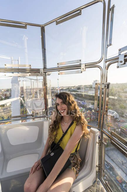 Positive female sitting in cabin of observation wheel and enjoying ride while having fun in amusement park and looking at camera — Stock Photo