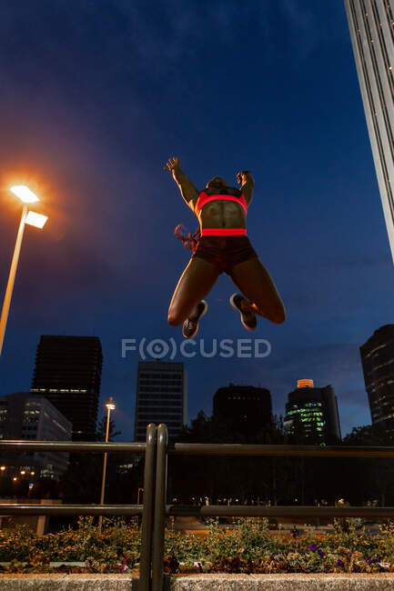 From below African American athletic woman jumping on street at night — Stock Photo