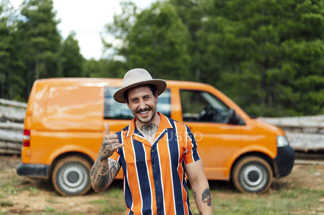 Viajero masculino serio apoyado en furgoneta estacionada en la naturaleza y mirando a la cámara durante la aventura de verano - foto de stock