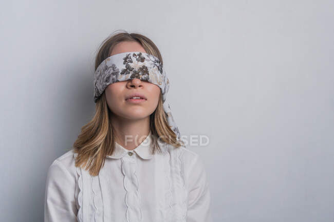 Giovane donna dai capelli biondi in camicetta elegante che copre gli occhi con sciarpa di seta piegata con ornamento floreale su sfondo bianco — Foto stock