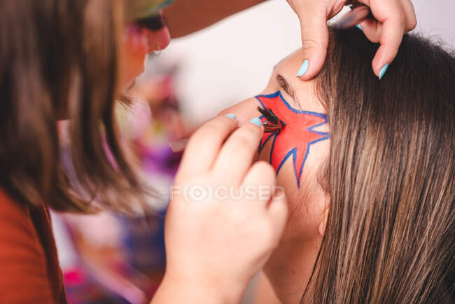 Artista de maquillaje de cultivos aplicando pestañas falsas en los párpados de la modelo femenina en el estudio - foto de stock