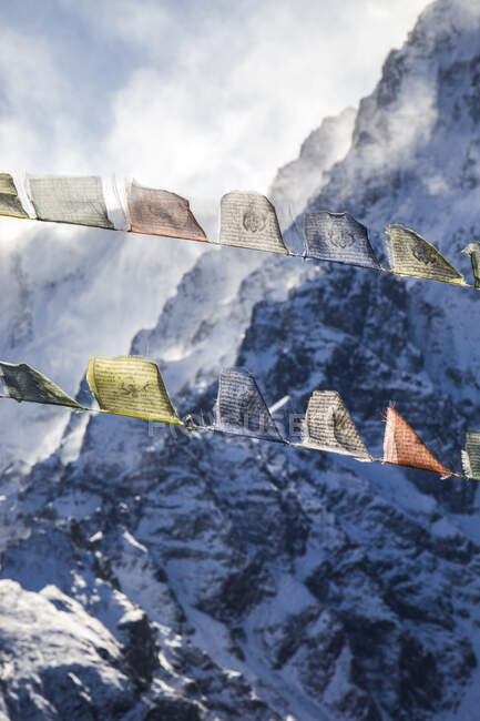 Linhas de bandeiras de oração budistas coloridas penduradas em cordas no fundo de Himalaias rochosos cobertos de neve no inverno no Nepal — Fotografia de Stock