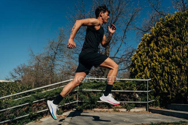 Vista laterale del jogger maschile attivo in abbigliamento sportivo che corre sulle scale durante l'allenamento sotto il cielo blu — Foto stock