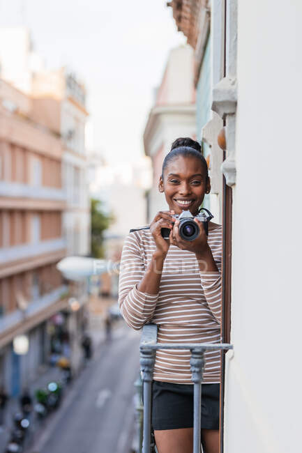 Content ethnic female in wear with striped ornament with professional photo device looking at camera on balcony in daytime — Stock Photo