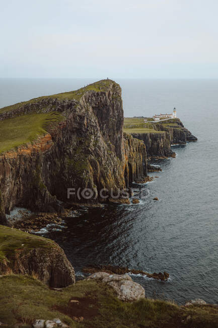 Жорсткий порослий травою скеля з маяком, розташований біля бурхливого моря в похмурий день у Великобританії. — стокове фото