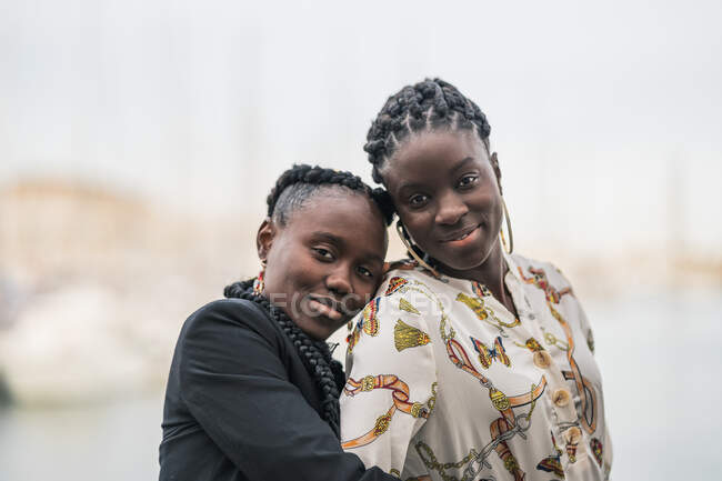 Contenu dames afro-américaines élégantes rester près et en regardant la caméra avec un sourire réfléchi dans le parc dans la journée lumineuse — Photo de stock