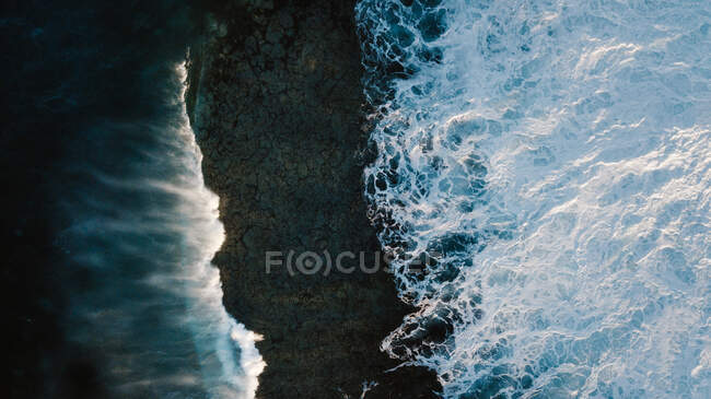 Drone view of breathtaking scenery of foamy sea waves crashing on rough rocky seashore — Stock Photo
