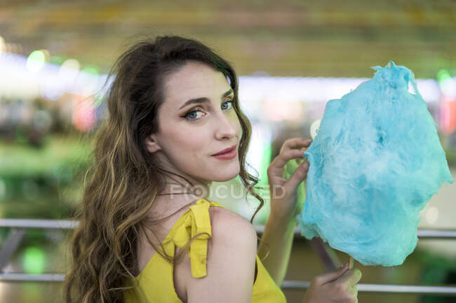 Vista lateral de la hembra infantil comiendo dulces de algodón azul dulce mientras se divierten y disfrutan de fin de semana en el recinto ferial en verano - foto de stock