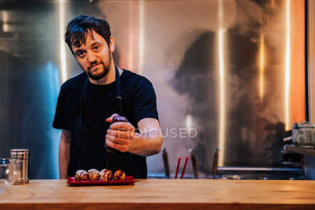 Chef gießt mit Gewürzen runde Fleischgerichte mit Sauce auf stilvollem Teller in Ramen-Bar — Stockfoto