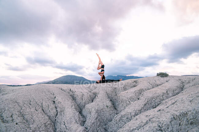 Вид сбоку женщины, балансирующей на руках мужчины во время сеанса акройоги в горах — стоковое фото